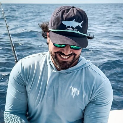 Man on a boat in the ocean wearing a cap and sunglasses, with a clear sky above.